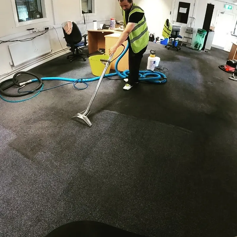 Technician performing hot water extraction carpet cleaning in an office