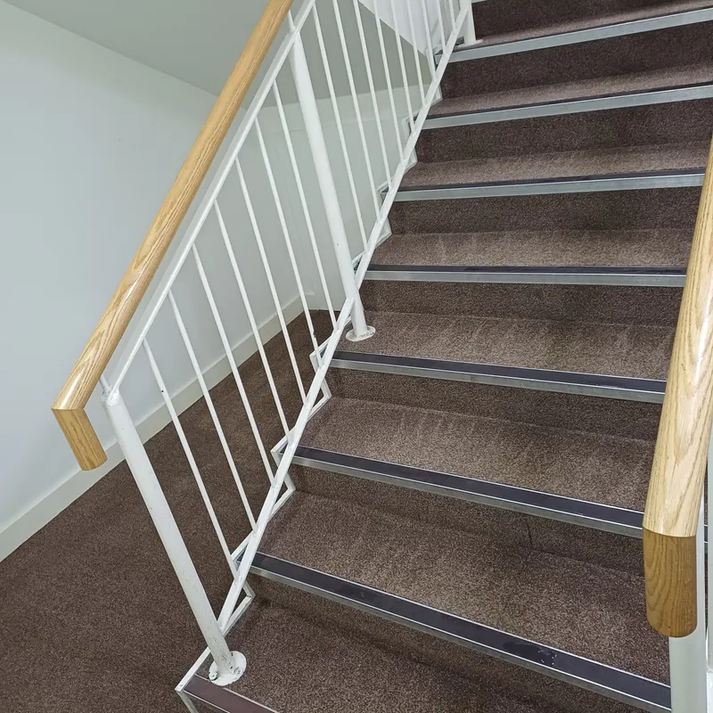 A grey carpeted staircase with white spindles and metal nosings