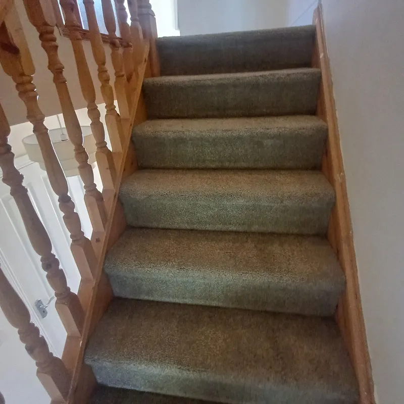 A grey carpeted staircase with a pine banister