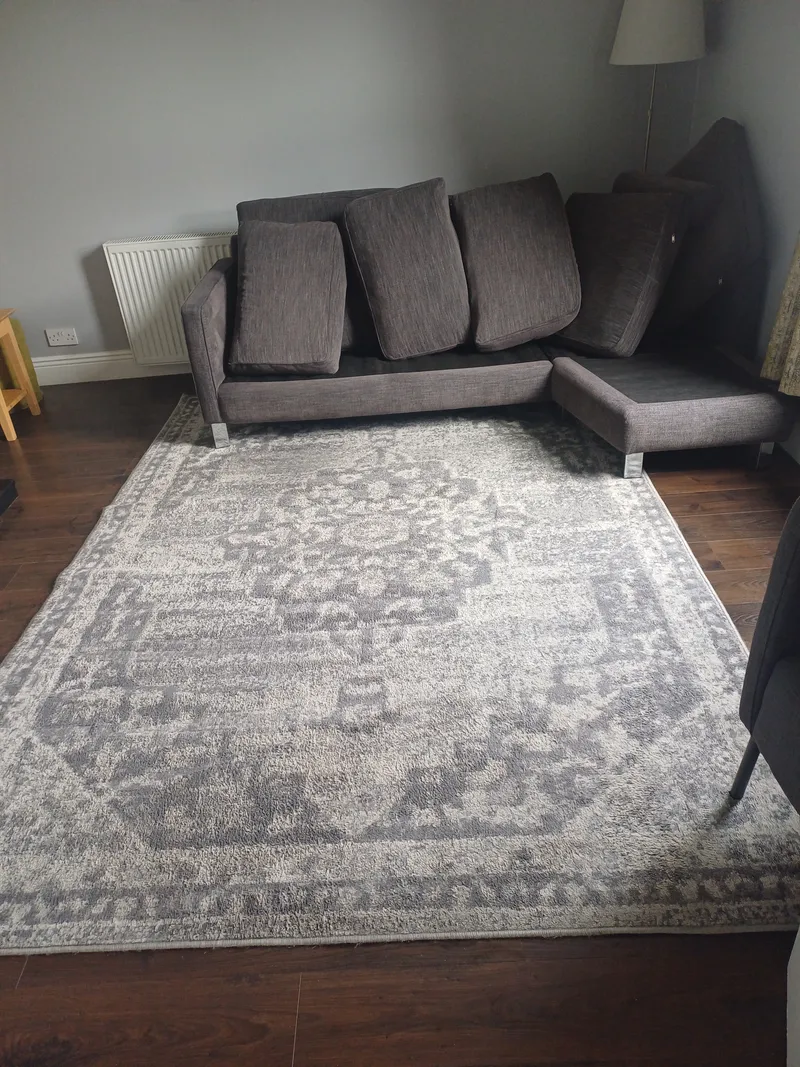 A grey and cream patterned rug laid in a living room in front of a grey corner sofa
