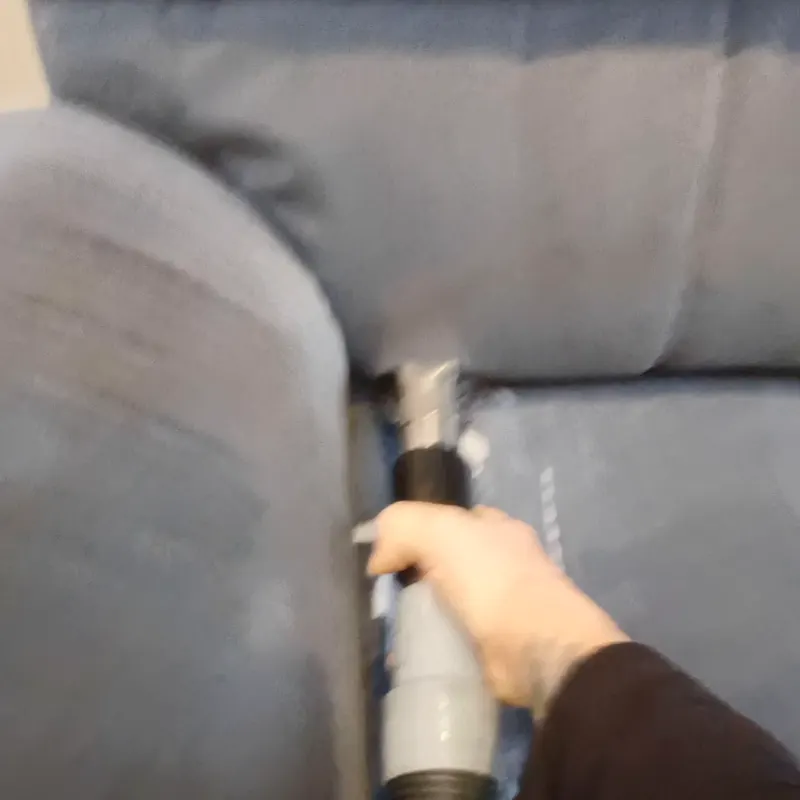 An upholstery cleaning tool being drawn down a grey fabric armchair