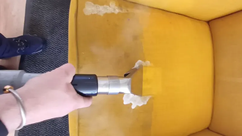 A yellow fabric wing armchair being cleaned with an upholstery tool