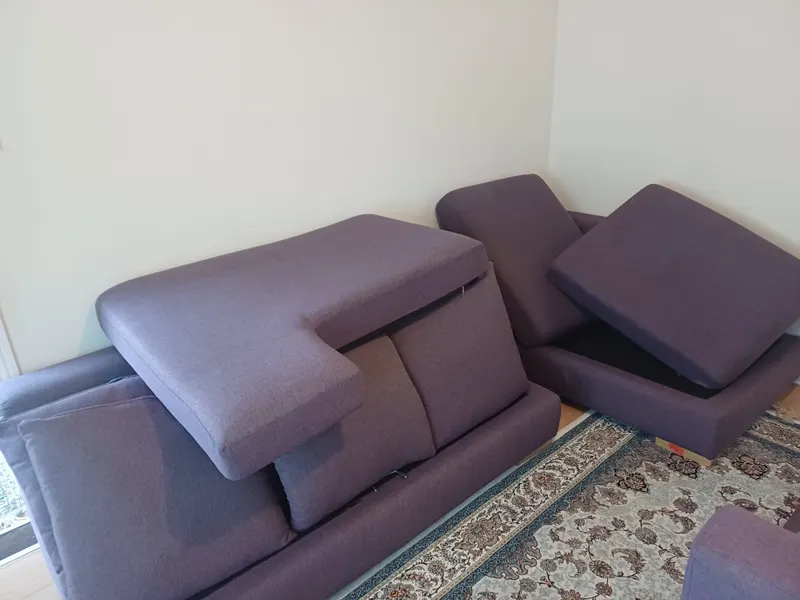 A purple fabric corner sofa with its cushions lifted to dry