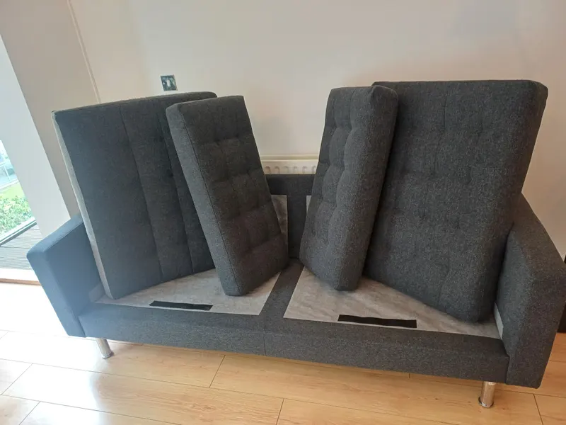 A dark grey sofa bed with its back cushions stood upright to dry