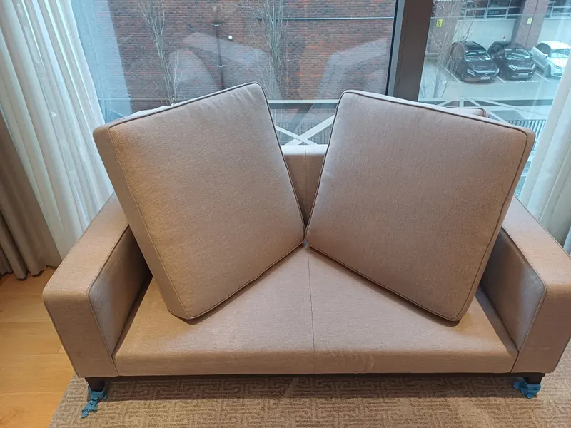 A tan fabric two-seater sofa with its seat cushions stood up to dry